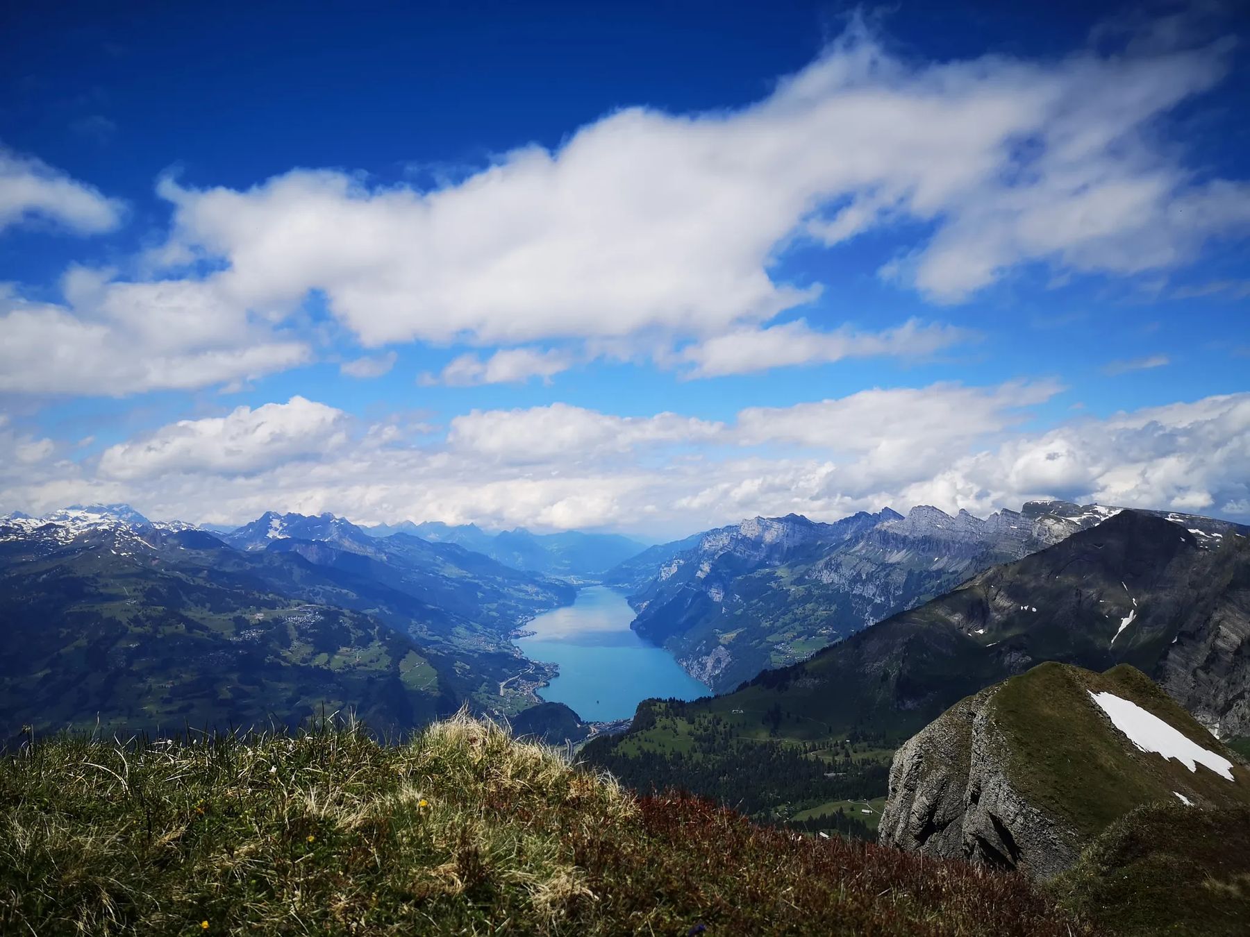 View from the summit of Alvier in the Swiss Alps, looking down a long blue lake between mountain ridges under a bright sky